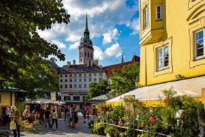Der Viktualienmarkt ist ein ständiger Markt für Lebensmittel in der Altstadt von München. Er findet seit 1807 täglich, außer an Sonn- und Feiertagen, statt. Das Erscheinungsbild des über zwei Hektar großen Geländes wird durch fest errichtete Buden mit zum Teil großen Auslagen geprägt. Dazu kommen einige saisonal unterschiedliche fliegende Stände. Die Marktstände sind in mehreren Abteilungen um einen Biergarten angeordnet. The Viktualienmarkt is a permanent market for food in the old town of Munich. It has taken place every day since 1807, except on Sundays and public holidays. The appearance of the over two hectare site is characterized by fixed stalls, some with large displays. There are also some seasonally different flying stands. The market stalls are arranged in several departments around a beer garden.